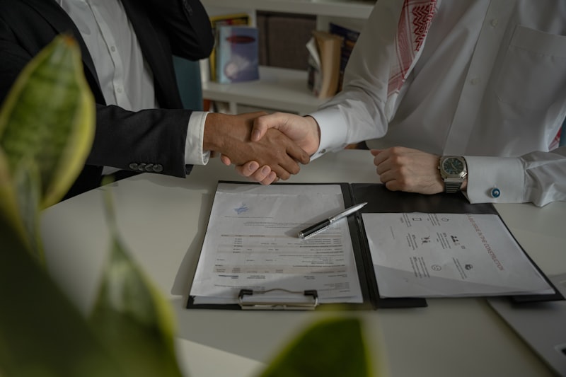 Two professionals shaking hands over signed financial agreement documents